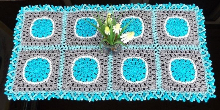 Rechteckiger gehäkelter Tischläufer aus acht Granny-Squares in Türkis, Grau und Weiß mit zackiger Kante und Glasvase mittig