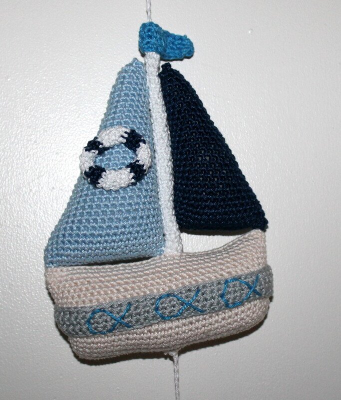 Gehäkeltes Segelboot mit hell- und dunkelblauen Segeln, beigem Rumpf, besticktem Band und kleinem Rettungsring