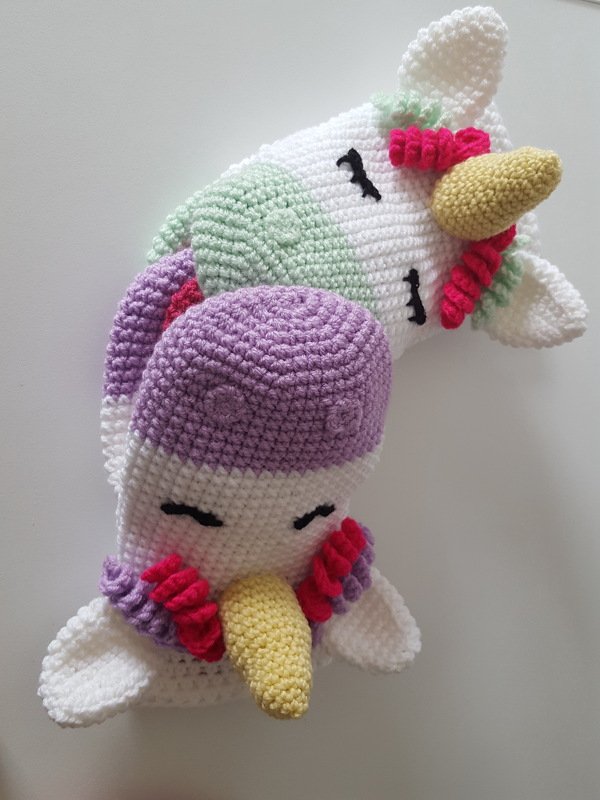 Zwei gehäkelte weiße Einhorn-Köpfe mit farbigen Mähnen und gelben Hörnern vor hellem Hintergrund.