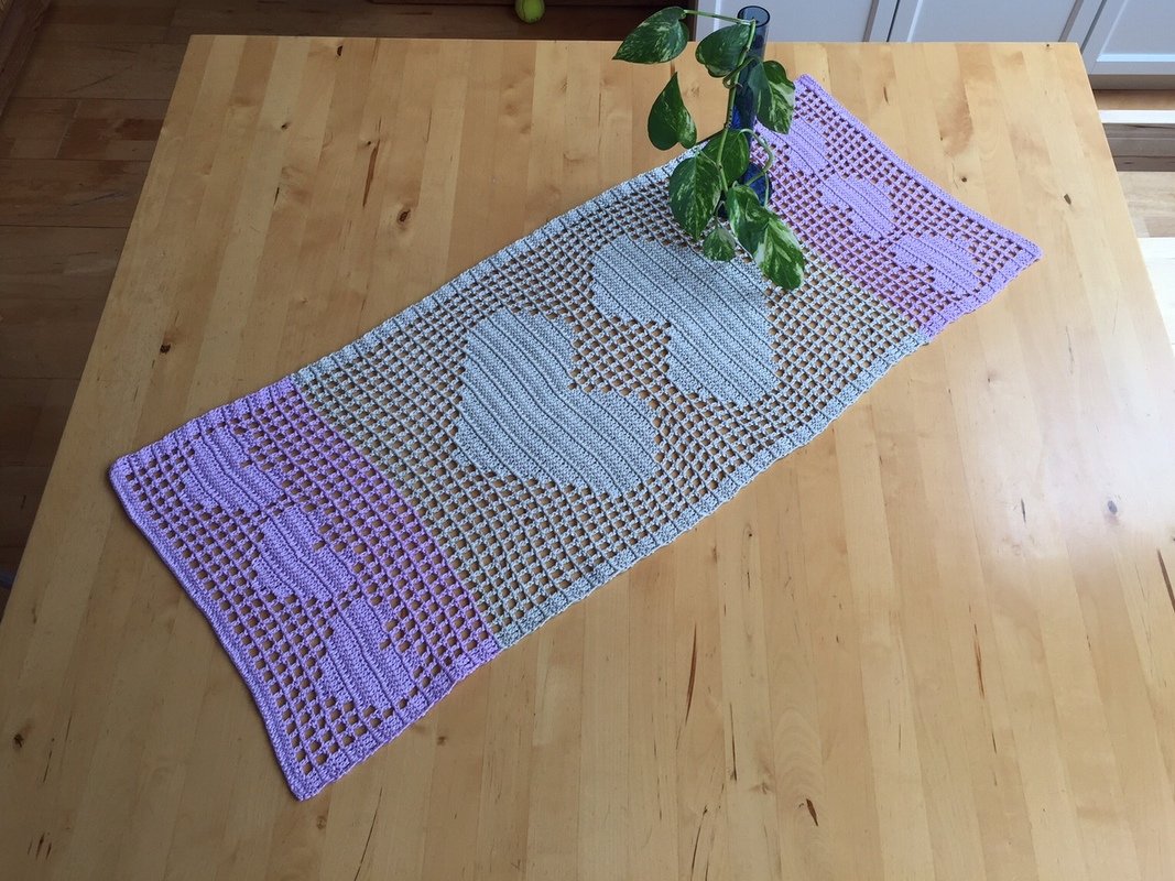 Rectangular crocheted filet table runner with two large central hearts and lavender end panels on a wooden table