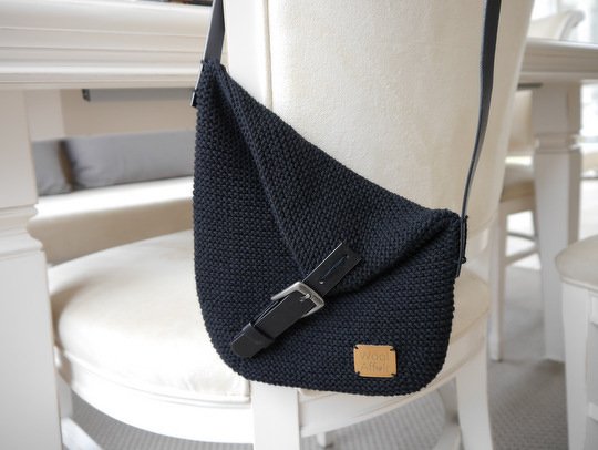 Schwarze gestrickte Umhängetasche mit Klappe und Schnallenverschluss an einem Stuhl
