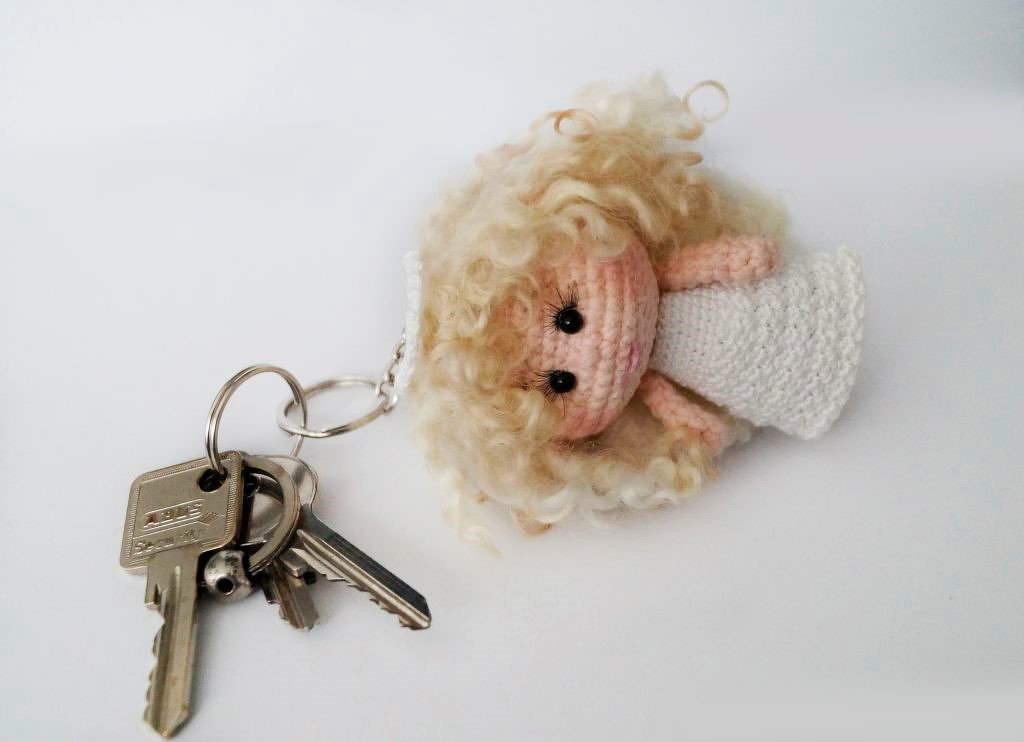 Crocheted amigurumi angel keychain with curly blonde hair and white dress attached to keys on a white background.