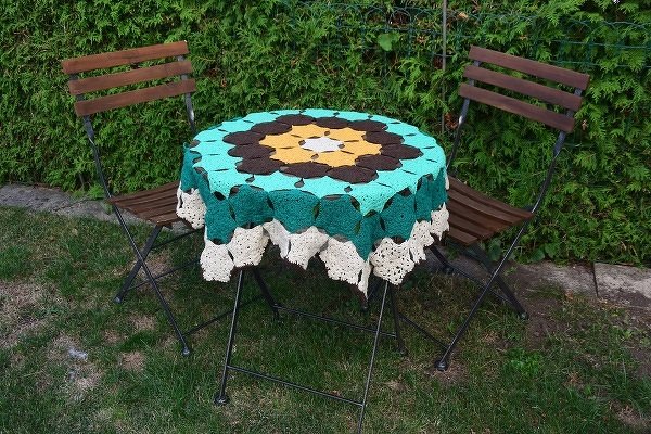 Rundes mehrfarbiges Häkeldeckchen mit floralem Muster auf kleinem Gartentisch