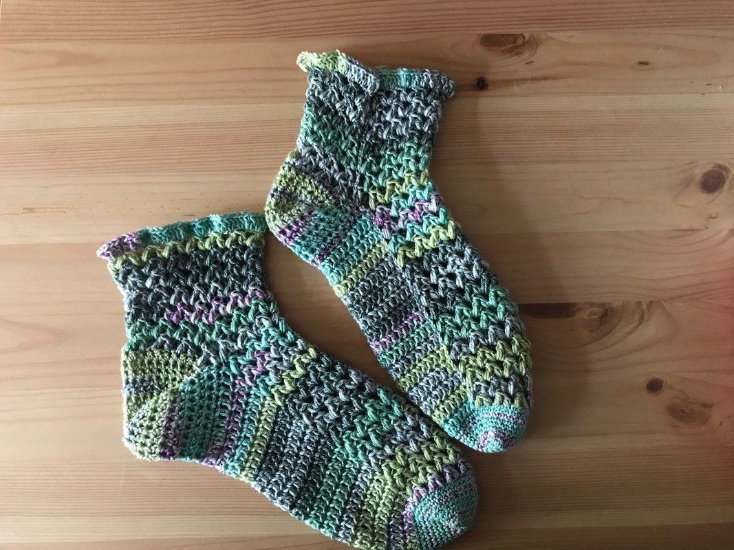 Paar gehäkelter Damensocken aus mehrfarbigem Farbverlaufsgarn auf Holztisch