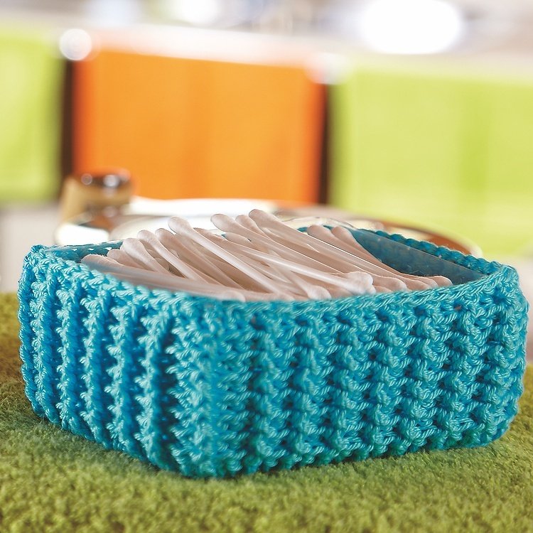 Türkiser gehäkelter Utensilo-Korb mit Wattestäbchen auf grünem Handtuch