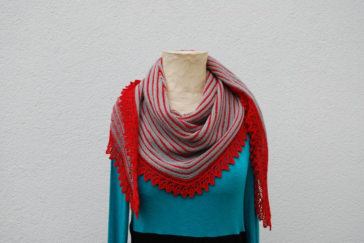 Gestreiftes Dreieckstuch in Rot und Grau mit roter Spitzenborte, drapiert auf einer Schaufensterpuppe über einem türkisfarbenen Oberteil.