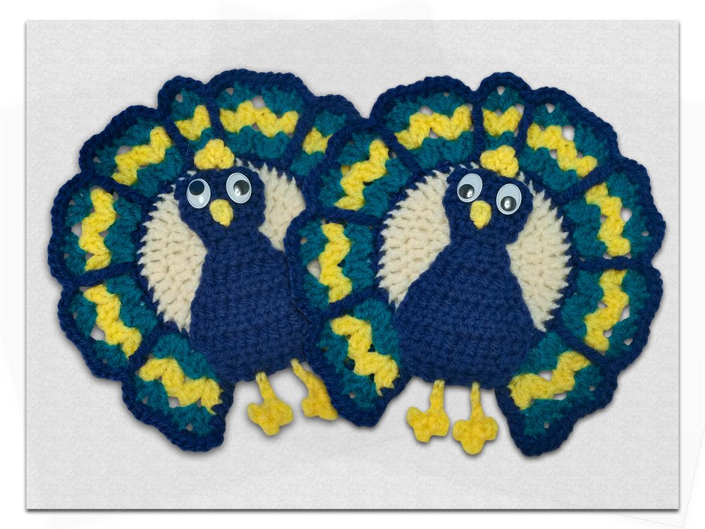 Zwei gehäkelte Pfau-Topflappen in Blau, Gelb und Türkis mit Wackelaugen.