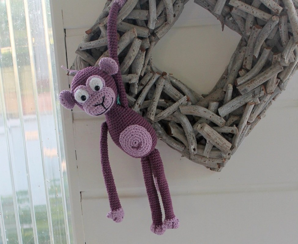 Lila gehäkelter Amigurumi-Affe an einem herzförmigen Astkranz