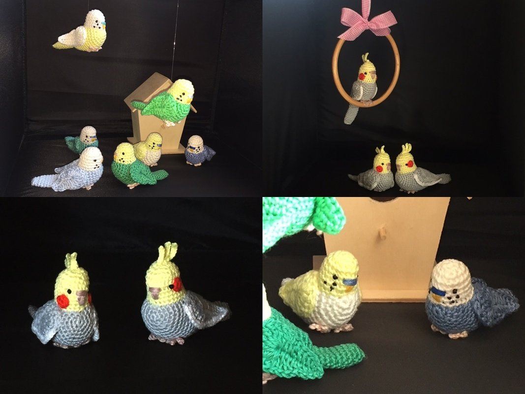 Mehrere gehäkelte Wellensittiche und Nymphensittiche, arrangiert mit Vogelhaus und Schaukelring vor dunklem Hintergrund.