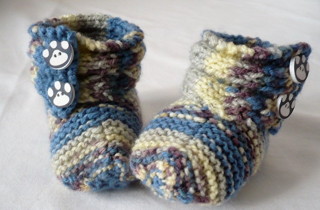 Gestrickte Babyschuhe blau-creme mit Pfotenknöpfen auf hellem Untergrund
