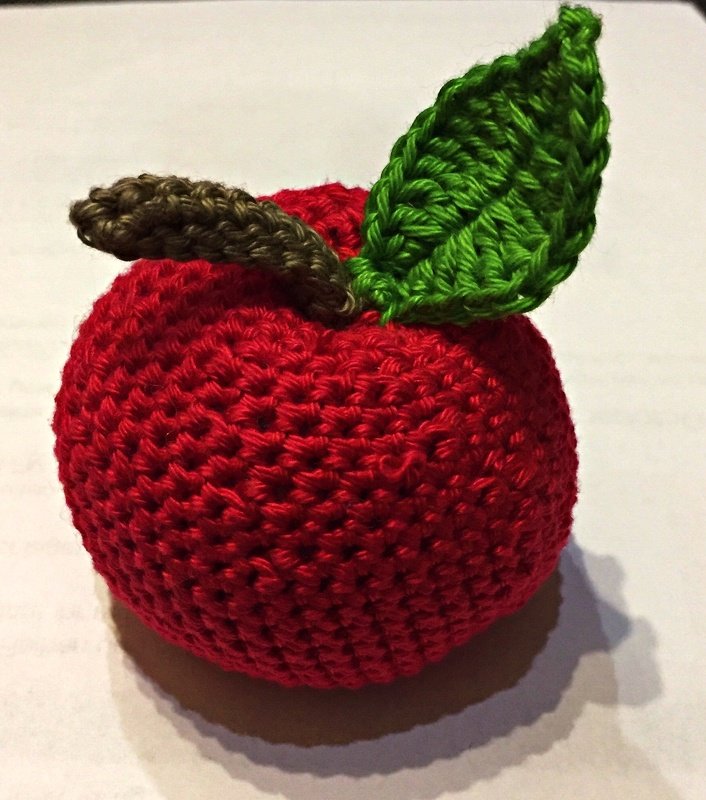 Gehäkelter roter Apfel aus Garn mit grünem Blatt und braunem Stiel auf hellem Untergrund