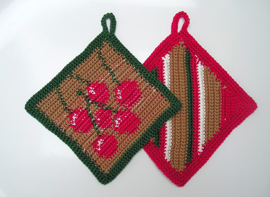 Zwei quadratische Topflappen mit Schlaufen, ein Motiv mit roten Beeren, das andere mit diagonalen Streifen