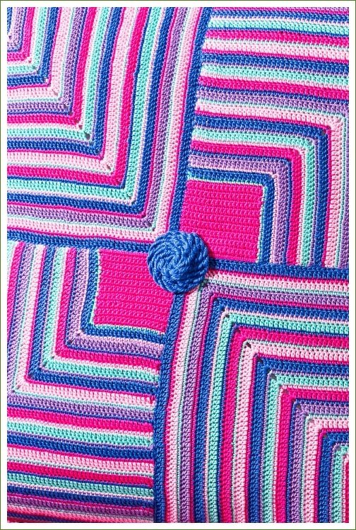 Gehäkelter Stoff in Pink, Blau, Mint und Violett mit konzentrischen Quadraten und rundem blauen Zierelement.