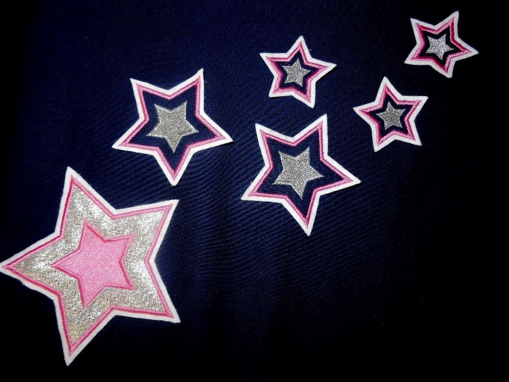 Mehrere gestickte Sterne in unterschiedlichen Größen mit pinker Mitte, silberner Füllung und weißer Umrandung auf dunkelblauem Stoff