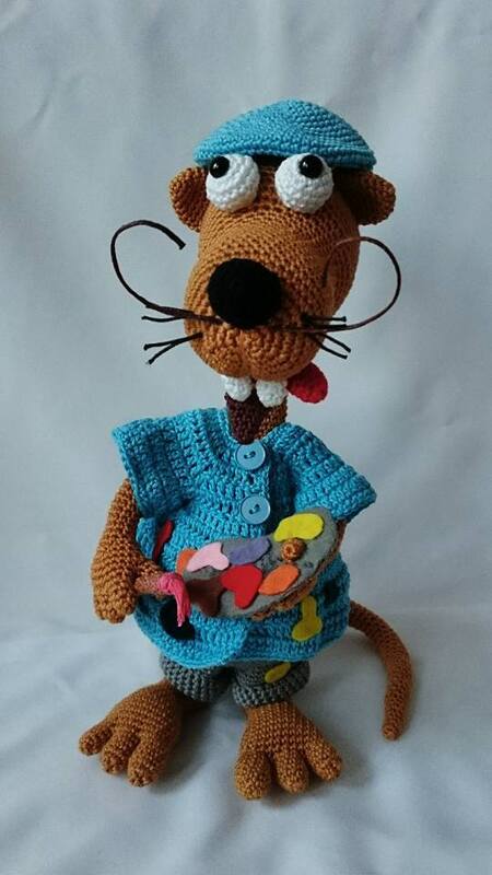 Gehäkeltes Amigurumi-Nagetier mit blauer Mütze und Outfit, hält Farbpalette und Pinsel.