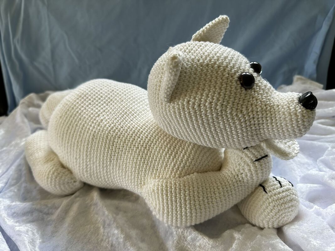 weiß gehäkelter Amigurumi-Bär liegend mit schwarzen Augen und Nase