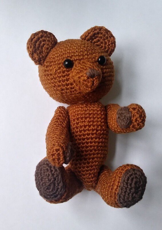 Brauner gehäkelter Amigurumi-Teddybär mit dunklen Pfoten und schwarzen Augen