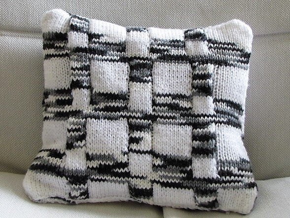 Gestricktes Kissen mit quadratischem Gittermuster in Schwarz, Weiß und Grau auf hellem Sofa