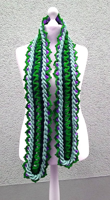 Gehäkelter Schal in Grün, Türkis und Lila auf weißer Schneiderpuppe mit strukturiertem Zopfrand.