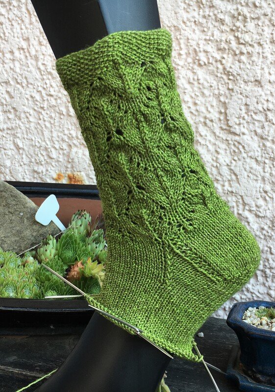 Grüne handgestrickte Socke in Arbeit mit Ajourmuster auf Strumpfform
