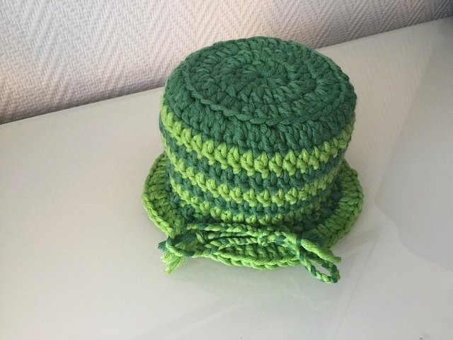 Zylindrisches gehäkeltes Utensilo mit horizontalen Streifen in Hellgrün und Dunkelgrün, mit Kordel am unteren Rand auf hellglatter Oberfläche.