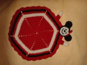 Sechseckiges gehäkeltes Schmusetuch in Rot, Weiß und Schwarz mit stilisierter Figurenapplikation und wellenförmigem Rand.