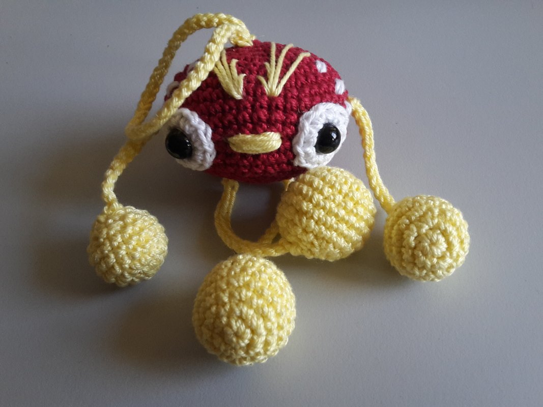 Gehäkeltes rotes Amigurumi mit gelben Kugeln und schwarzen Augen