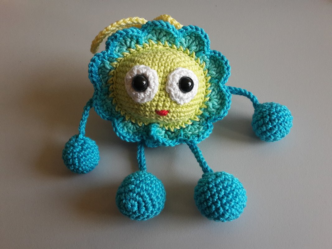 Rundes gehäkeltes Amigurumi in Gelb mit türkisfarbener Borte, großen Augen und vier gehäkelten Kugeln