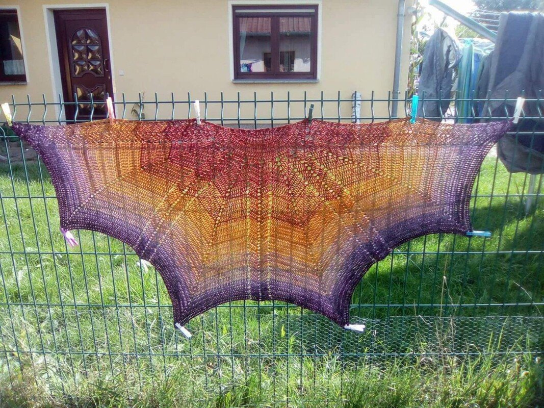 Gehäkeltes Tuch in Lila, Orange und Rotbraun mit Spitzen- und Lochmuster an einem Gartenzaun