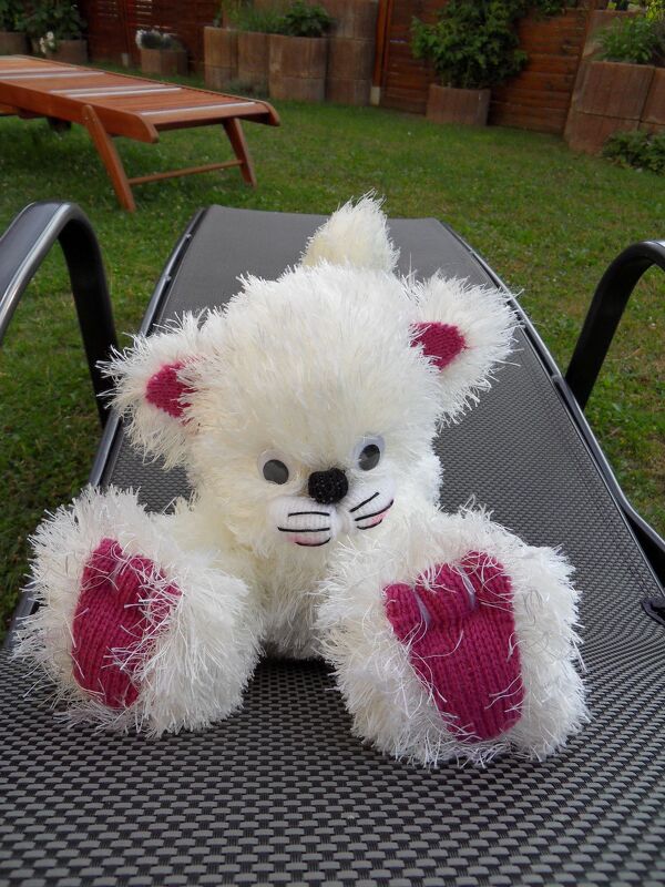 Weißes flauschiges Amigurumi-Tier mit pinken Ohren und Pfoten auf Gartenliege