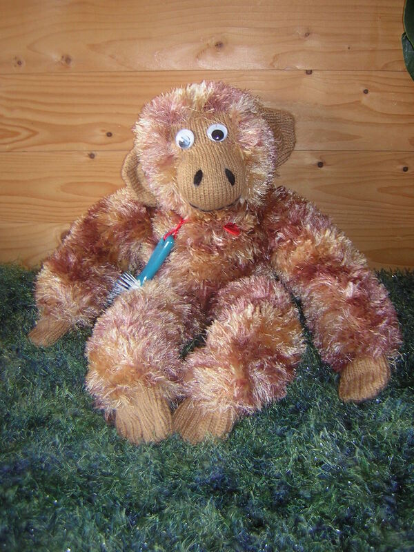 Gestrickter flauschiger Amigurumi-Affe mit Wackelaugen und roter Schleife auf grünem Teppich