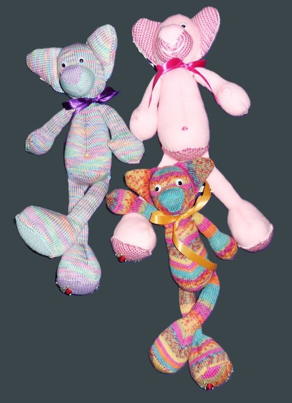 Drei handgestrickte Amigurumi‑Elefanten in Pastell, Rosa und Regenbogenstreifen mit Schleifen
