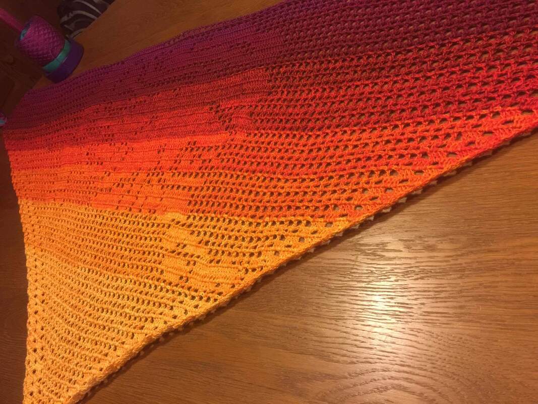 Gehäkeltes dreieckiges Tuch mit Farbverlauf von Gelb über Orange zu Rot, Loch- und Motivstreifen, auf Holztisch