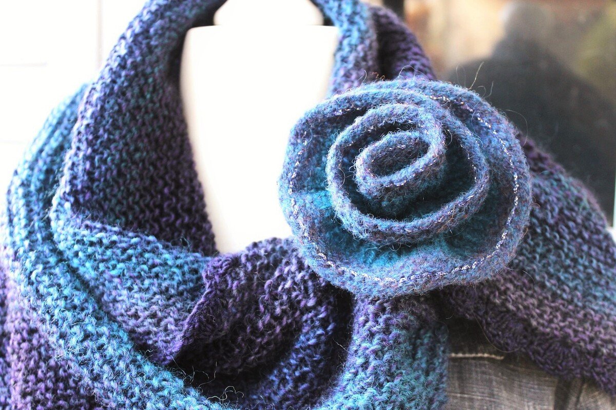 Knitted triangle shawl in blue and purple with a flower brooch on a mannequin