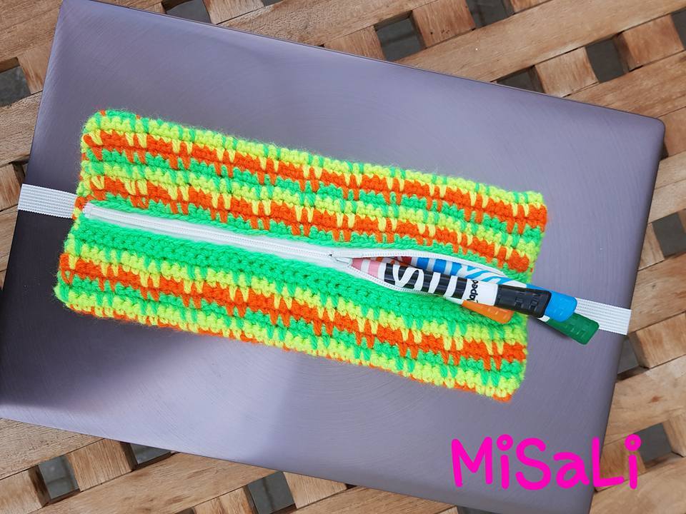 Gehäkeltes Mäppchen in Neongrün, Orange und Gelb mit weißem Reißverschluss auf einem Laptop