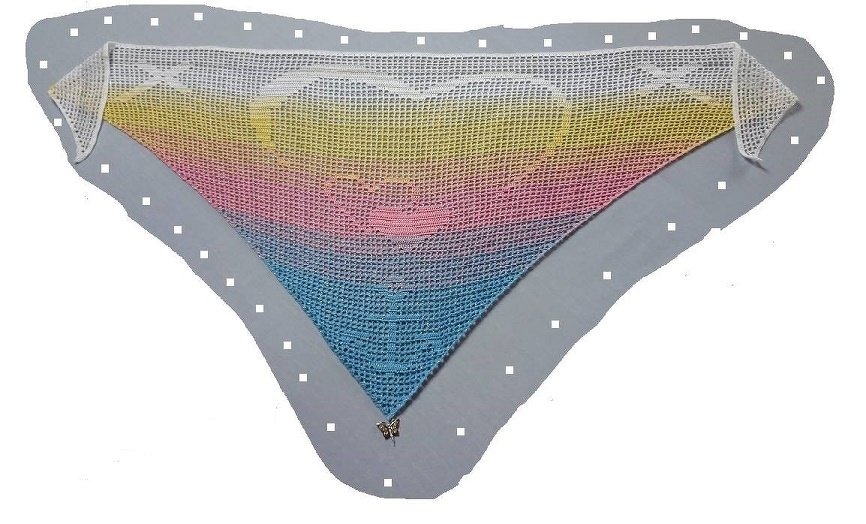 Dreieckiges Häkeltuch mit Farbverlauf in Weiß, Gelb, Rosa und Blau, Herzmotiv und Schmetterlingsanhänger.