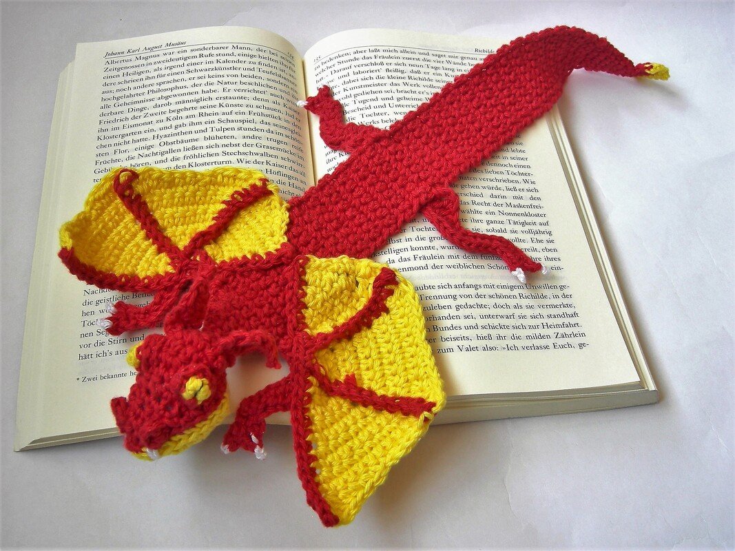Handgehäkeltes rot-gelbes Drachen-Lesezeichen liegt in einem offenen Buch