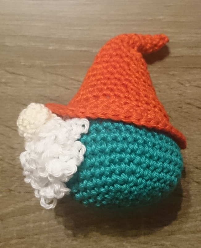 Gehäkelter Wichtel mit oranger Zipfelmütze, türkisfarbenem Körper und weißem Bart
