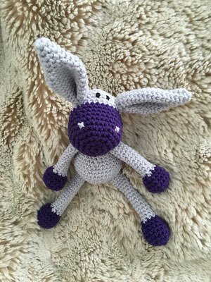 Nahaufnahme eines gehäkelten Amigurumi-Häschen mit sichtbarer Maschenstruktur, langen Ohren und lila Farbakzenten