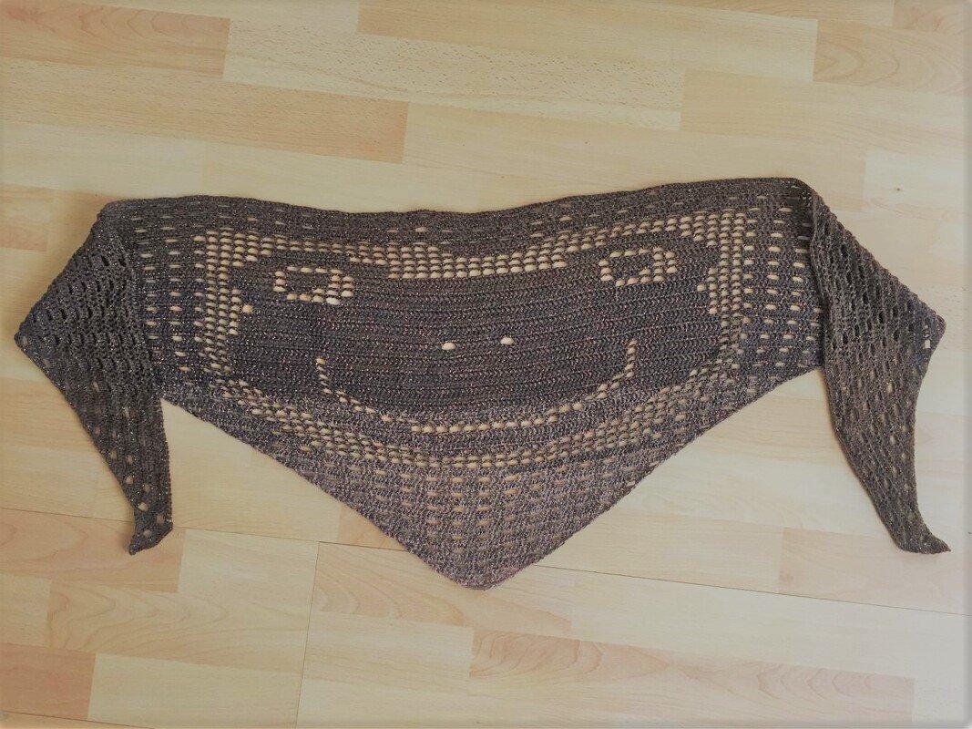 Dreieckiges gehäkeltes Kindertuch in Dunkelgrau mit Smiley-Lochmuster auf hellem Holzboden