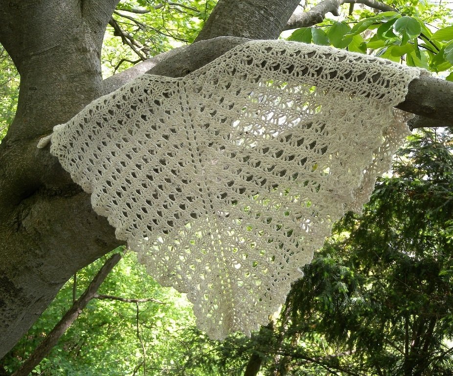 Cremefarbenes, dreieckiges gehäkeltes Lacetuch mit Muschelrand an einem Baumast drapiert