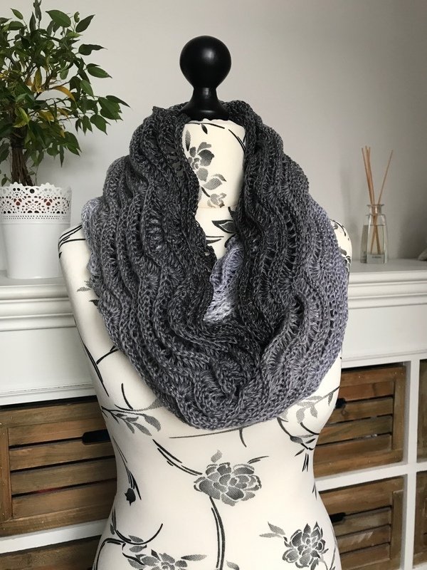 Gehäkelter Loop-Schal in abgestuften Grautönen mit Wellenstruktur auf einer Schneiderpuppe