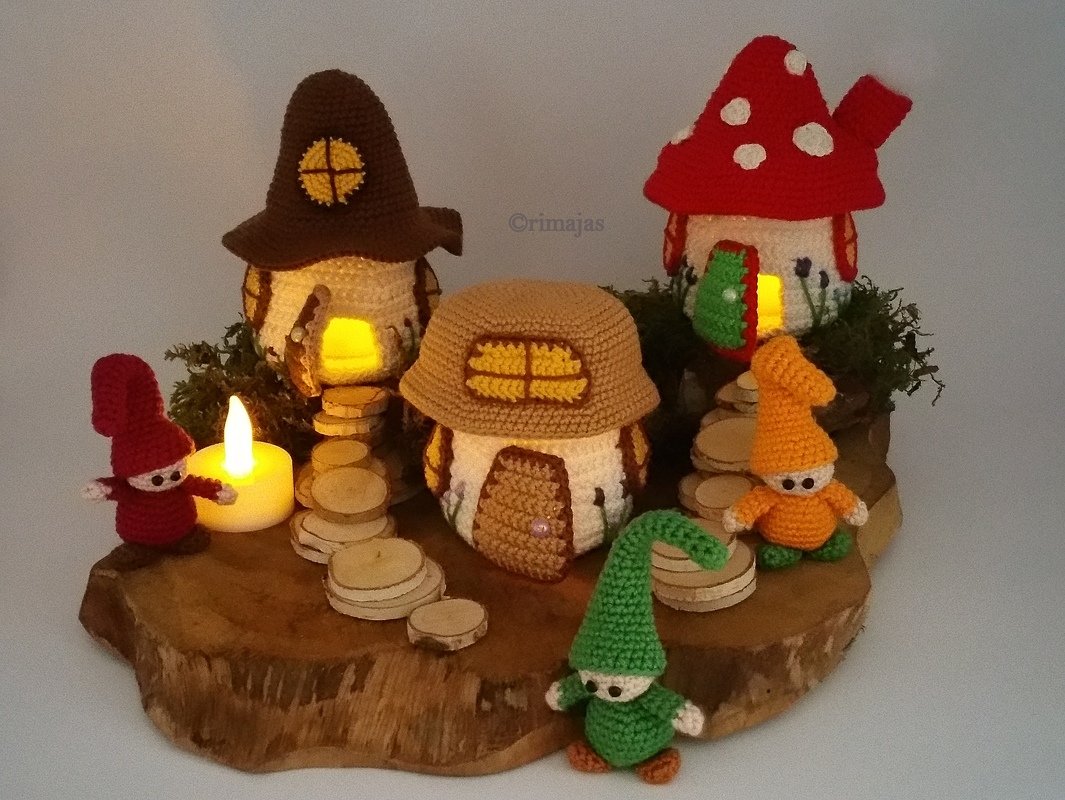 Handgehäkelte, innen beleuchtete Häuschen und kleine Wichtelfiguren auf einer Holzscheibe