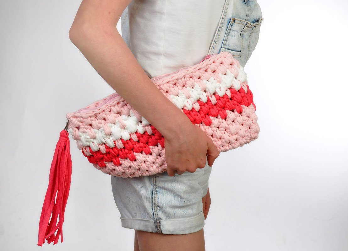 Gehäkelte Clutch in Rosa, Weiß und Rot mit Reißverschluss und Quaste, an der Hüfte gehalten.