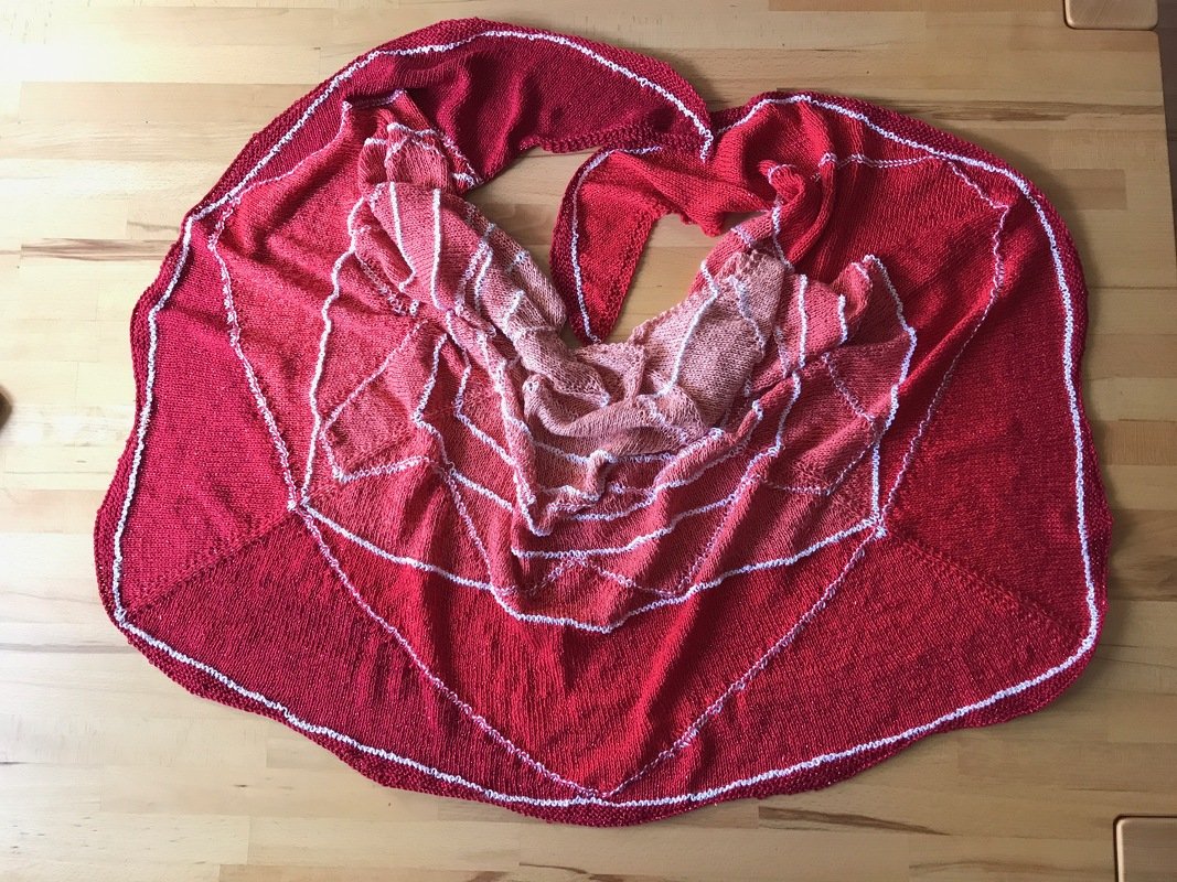 Halbmondförmiges gestricktes Tuch in Rot- und Pinktönen mit weißen Maschenreihen auf Holzuntergrund