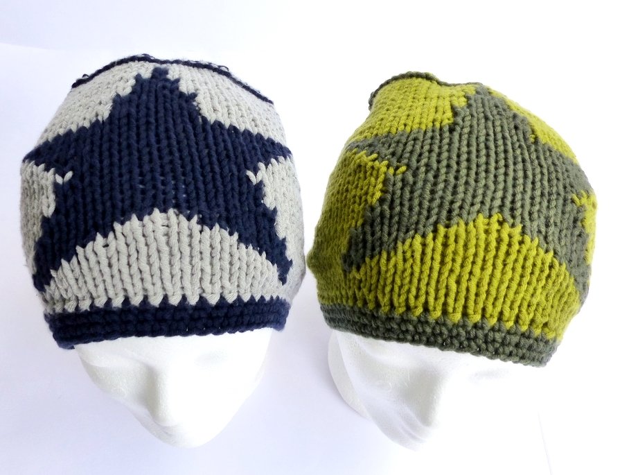 Zwei gestrickte Beanies mit kontrastierendem Sternmuster auf weißen Schaufensterköpfen; links dunkelblau/hellgrau, rechts olivgrün/gelbgrün