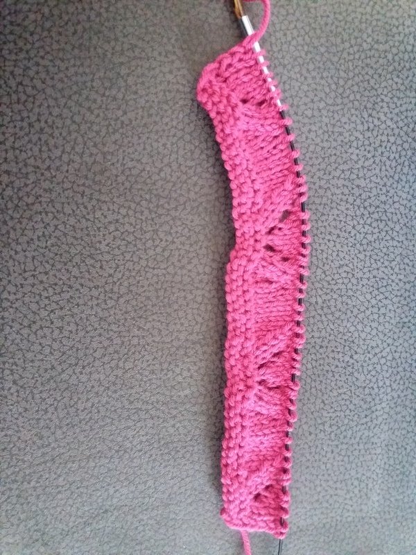 Gestrickter rosa Musterstreifen mit Lochmuster auf Stricknadeln.