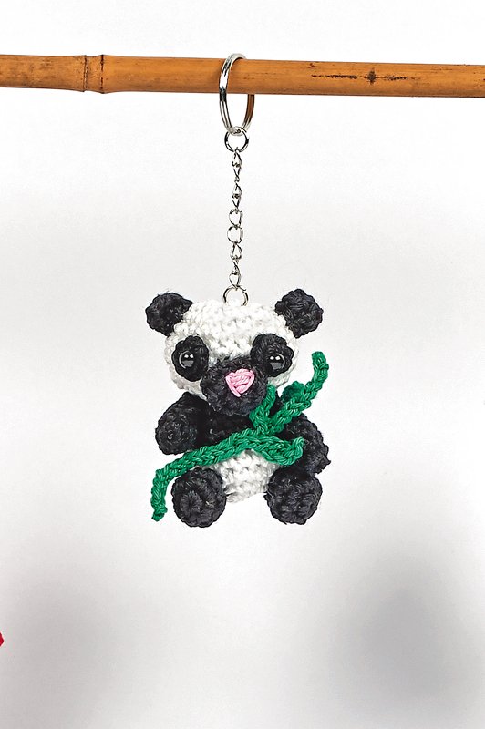 Gehäkelter Panda-Schlüsselanhänger in Schwarz-Weiß mit grünem Bambuszweig, an Metallkette und Schlüsselring hängend.