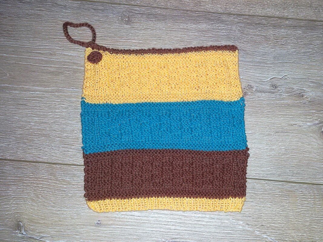 Quadratischer gestrickter Topflappen mit horizontalen Streifen in Gelb, Türkis und Braun und Aufhängeschlaufe oben links.