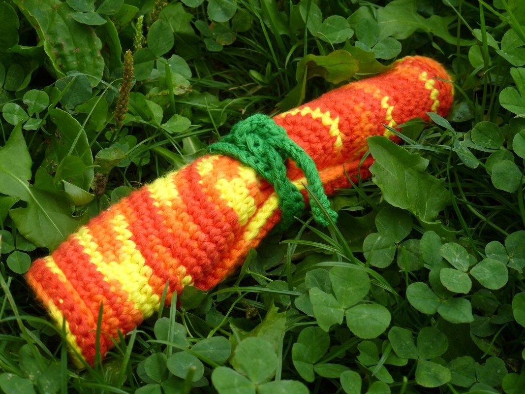 Gehäkelte Möhre in Orange und Gelb mit grünem Band auf grünem Gras.